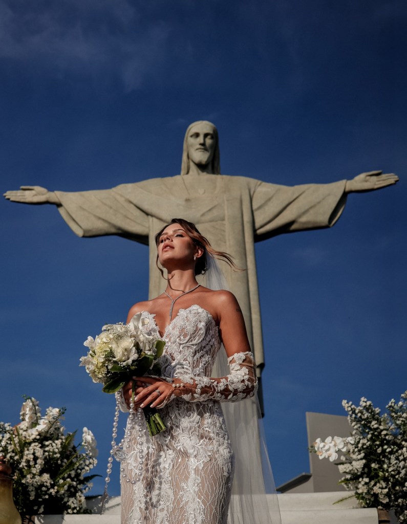 Bride holding a bouquet during a wedding ceremony beneath Christ the Redeemer statue in Rio de Janeiro, Brazil