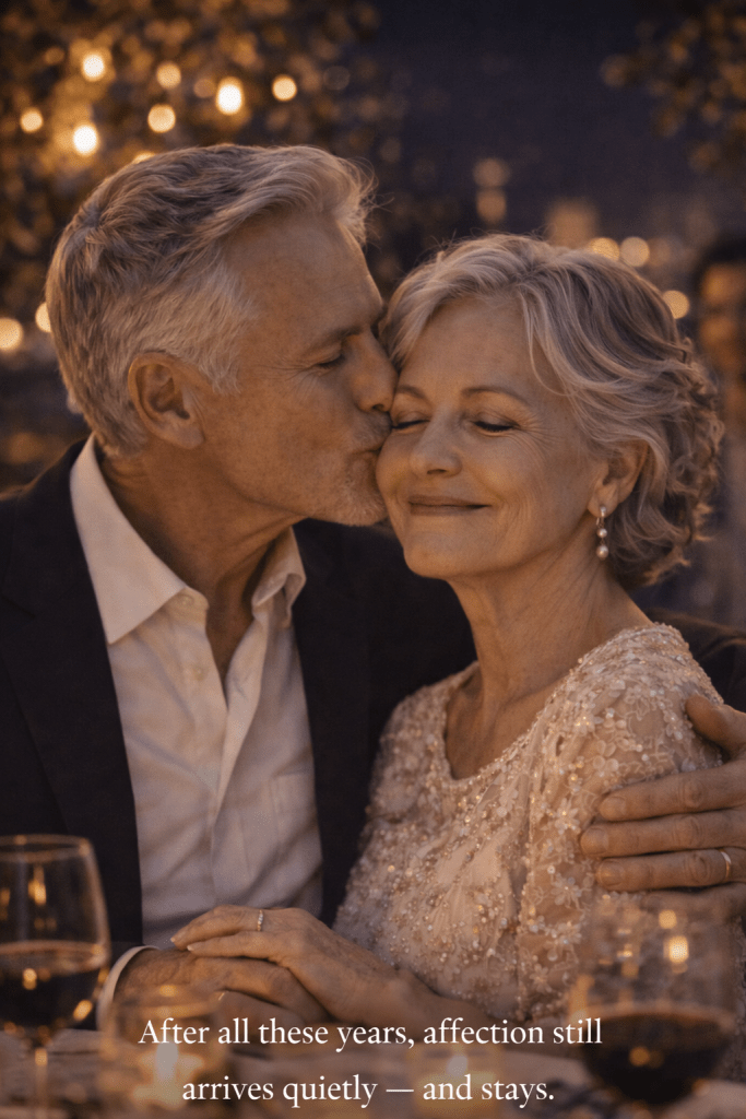 An elderly man kissing his wife on the cheek during an intimate anniversary celebration at night.