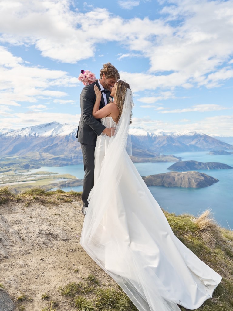 Bride and groom embracing on a mountain overlooking a lake in New Zealand during an intimate wedding