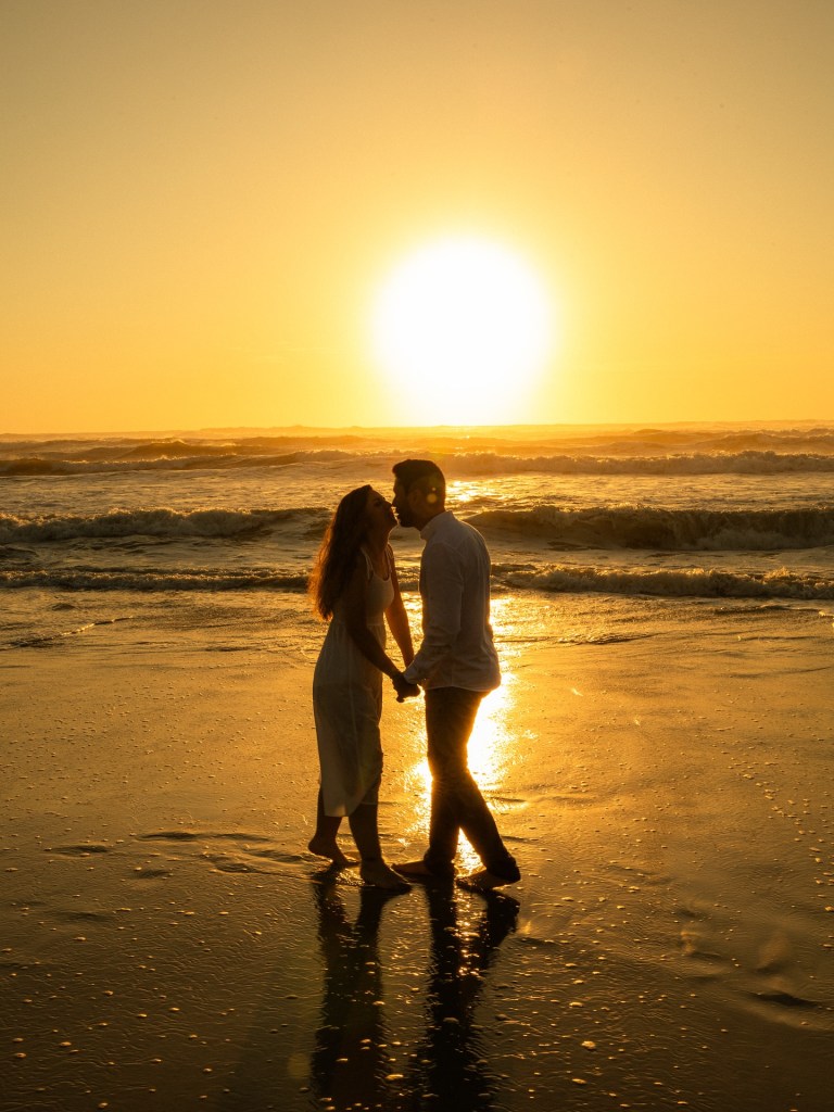 A couple holding hands at sunset on the beach, silhouetted by golden light, symbolizing love, connection, and a shared journey together