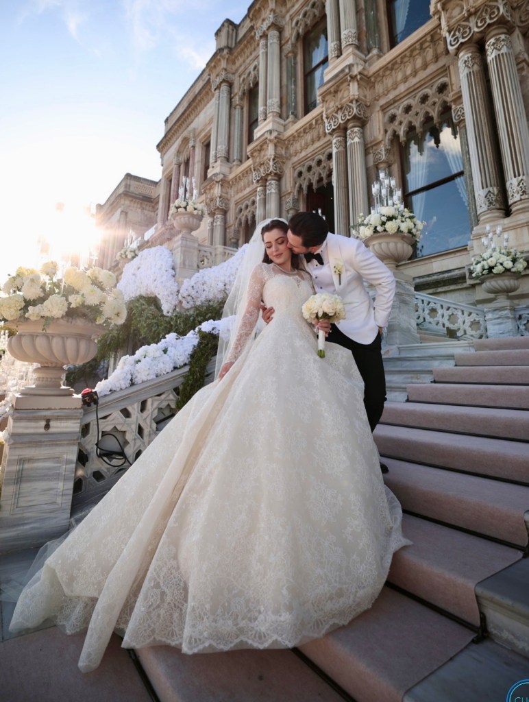 Elegant wedding couple embracing on the grand staircase of a historic palace in Istanbul, Turkey, surrounded by white floral arrangements.